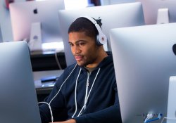 Student wearing headphones while using large-screen computer in computer lab.