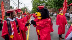 Deacon the bear wearing cap and gown, shakes hands with a graduate