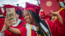 graduate takes a selfie holding up a red diploma holder