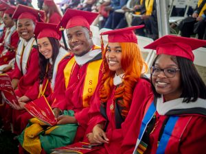 row of Bloomfield graduates in red caps and gowns smiling for the camera 