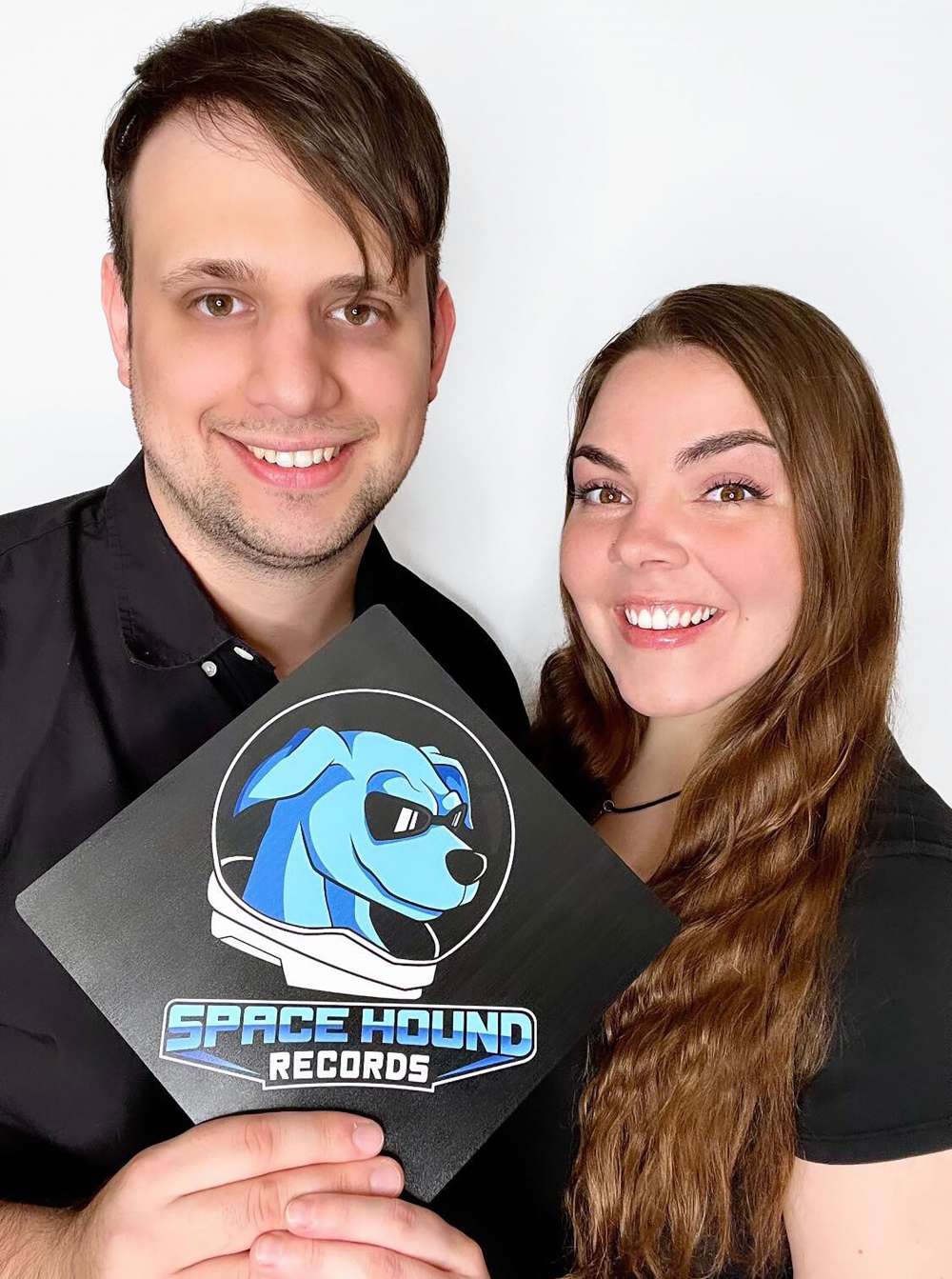 Corey Morgart and Therese Sheridan hold a sign that says Space Hound Records with a logo of a dog wearing a space helmet.